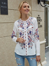 Load image into Gallery viewer, Woman wearing a white blouse with colorful embroidery standing in front of a building.