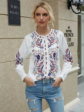 Load image into Gallery viewer, Woman wearing a white blouse with colorful embroidery and ripped jeans standing in front of a building.