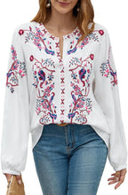 Load image into Gallery viewer, Woman wearing a white blouse with colorful floral embroidery and blue jeans.