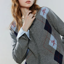 Load image into Gallery viewer, A close-up of a woman wearing a gray button-front cardigan with an argyle pattern in light blue, navy, and red, layered over a light blue collared shirt.