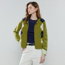 Load image into Gallery viewer, A woman models a green argyle cardigan with navy and white diamond patterns, worn over a navy blue top and white pants against a light gray studio background
